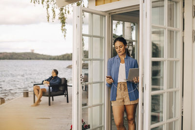 Mature woman using mobile phone and laptop with man in background