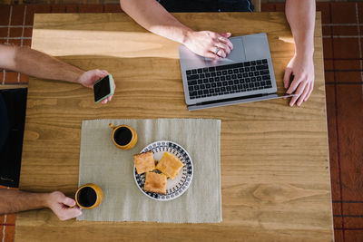 People, laptop, phone and breakfast on a wooden table.