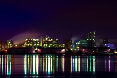 Illuminated buildings by river against sky at night