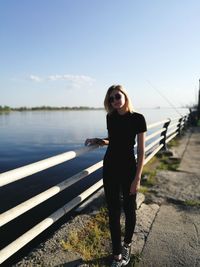 Portrait of young woman standing by railing against sky