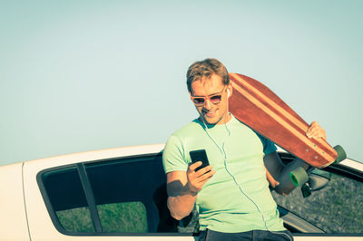 Young man using mobile phone while standing on car