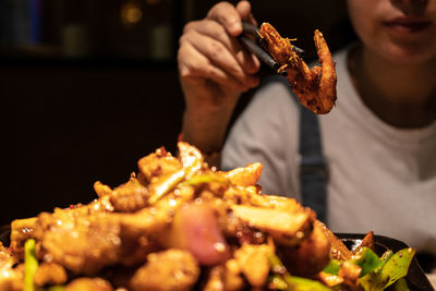 Midsection of woman holding fried shrimp in chopsticks at restaurant