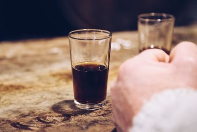Close-up of hand beside a glass of sherry on wooden shelf 