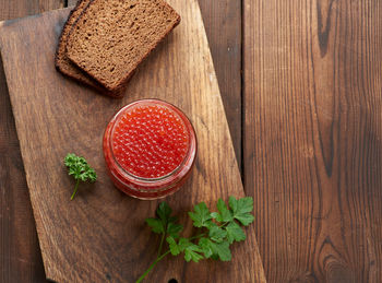 Full glass jar with red caviar on a brown wooden table, top view