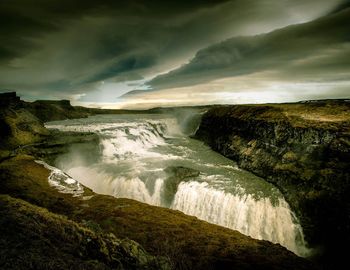 Scenic view of waterfall against cloudy sky