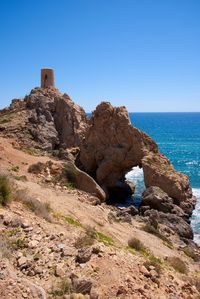 Rocks by sea against clear blue sky