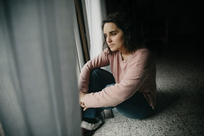 Woman looking away while sitting on floor