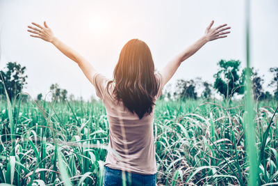 Rear view of woman standing with arms outstretched on field against sky