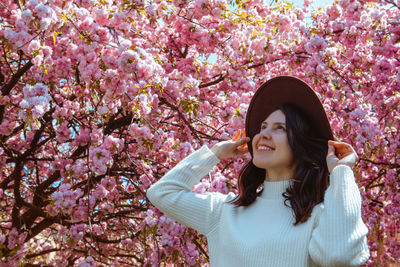 Portrait of young woman standing by cherry blossom