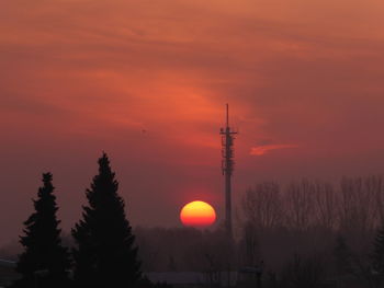 Low angle view of communications tower against orange sky