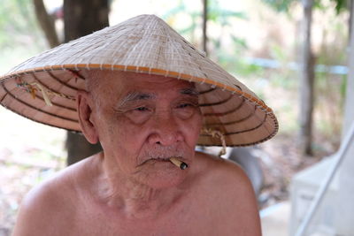 Shirtless senior man smoking cigarette while sitting outdoors