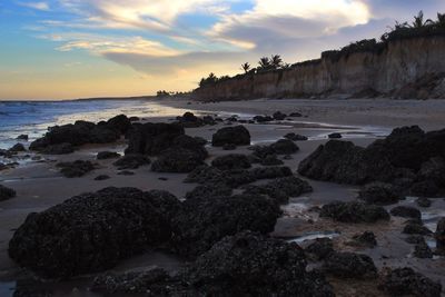 Rocks on beach against sky during sunset