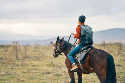 Rear view of man riding horse on field