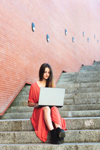 Beautiful young woman using laptop while sitting on staircase
