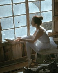 Side view of woman sitting on window at home