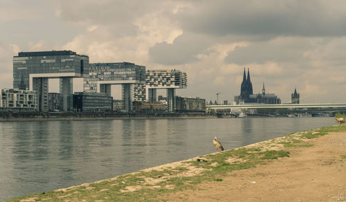 Buildings by river against cloudy sky