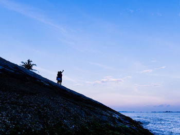 Man standing on rock by sea against sky