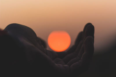 Optical illusion of hand holding sun at sunset