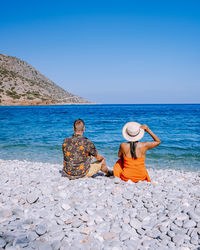 Rear view of couple sitting on rock by sea against sky