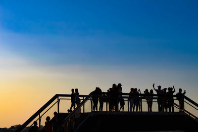 Silhouette people standing by railing against sky during sunset