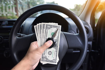 Cropped hand holding key with paper currency in car