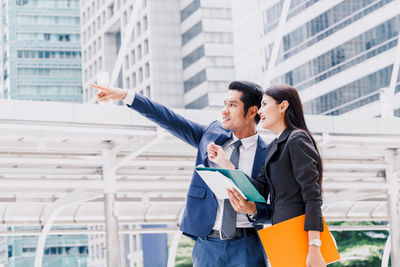 Colleagues discussing while standing against buildings in city