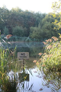 Sign board by lake against trees