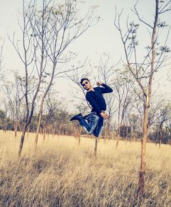 Full length of man jumping against bare trees