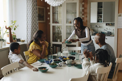 Girl serving food to family sitting at dining table