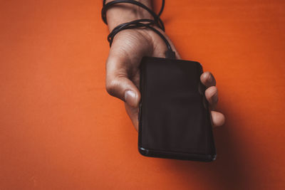 Midsection of man using smart phone against orange background