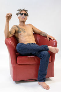 Shirtless wearing sunglasses while smoking cigarette against white background
