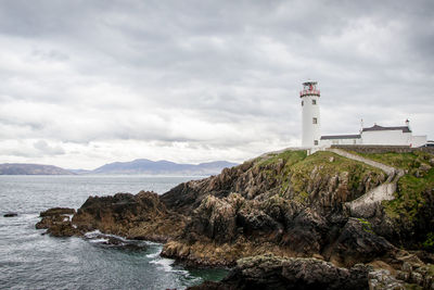 Lighthouse by sea and buildings against sky