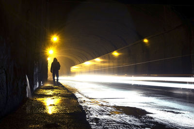 Rear view of silhouette man walking on illuminated street at night