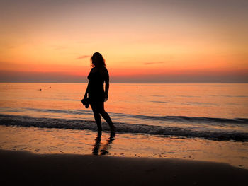 Silhouette woman standing on beach against sky during sunset