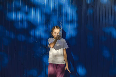 Sunny splashes, teenage girl radiates joy against a vivid blue wall