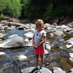 Full length portrait of girl standing on rock at river 