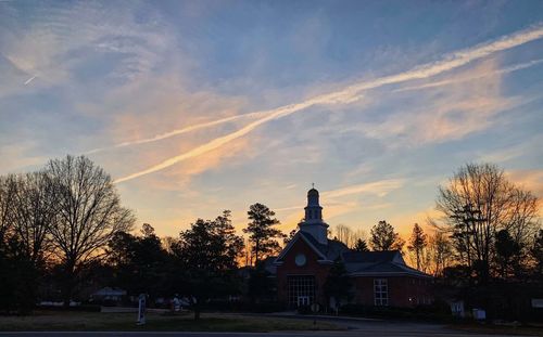 Trees by building against sky during sunset