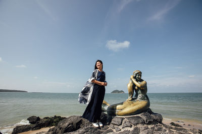 Young woman sitting on rock by sea against sky