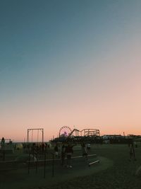 People at amusement park against sky during sunset