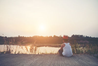 Rear view of boy sitting on pier in lake against sky