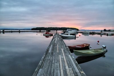 Pier by boats moored lake during sunset