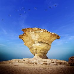 Birds flying over rock formation against blue sky