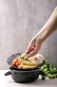 Cropped hand of woman with vegetables against wall