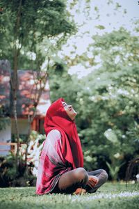 Side view of woman sitting on plant against trees