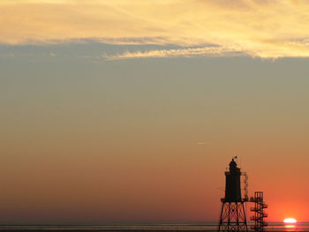 Silhouette lighthouse by sea against orange sky