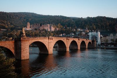 Arch bridge over river in city against clear sky