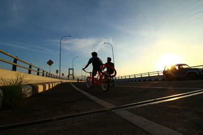 Low angle view of men riding bicycle on street during sunset