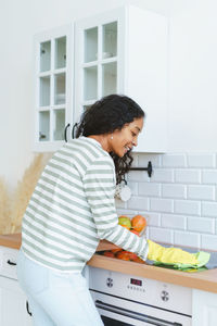 Back view of african-american female cleaning induction stove in rubber gloves with washcloth