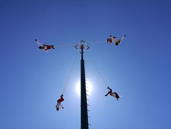 Low angle view of people on rope against clear blue sky