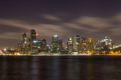 Illuminated buildings by sea against sky at night